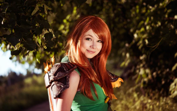 A woman in a vibrant Windranger cosplay from DotA 2 stands confidently outdoors, showcasing her detailed costume against a lush background. This HD image serves as an impressive desktop wallpaper.