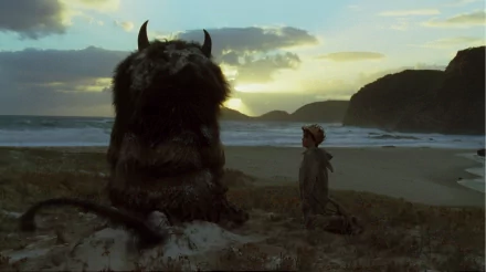 HD PC desktop wallpaper: scene from the movie Where the Wild Things Are — boy in a raincoat faces a large furry monster on a windswept beach at sunset.