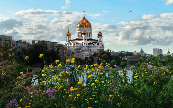 4K Ultra HD image of the Cathedral of Christ the Saviour with golden domes behind a vibrant field of wildflowers under a partly cloudy sky.