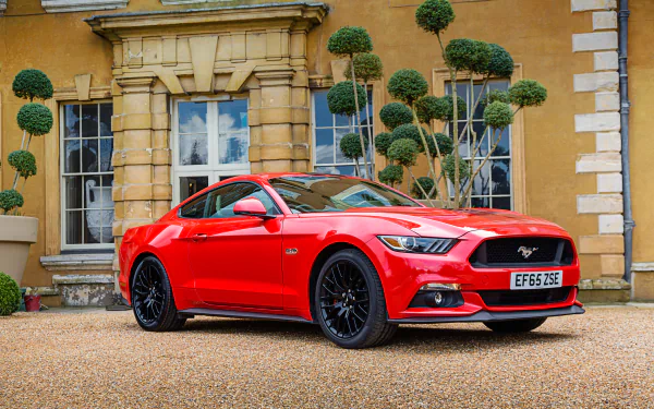 Red Ford Mustang GT muscle car parked in front of a historic stone building, captured in vivid 4K Ultra HD for a striking desktop wallpaper background.