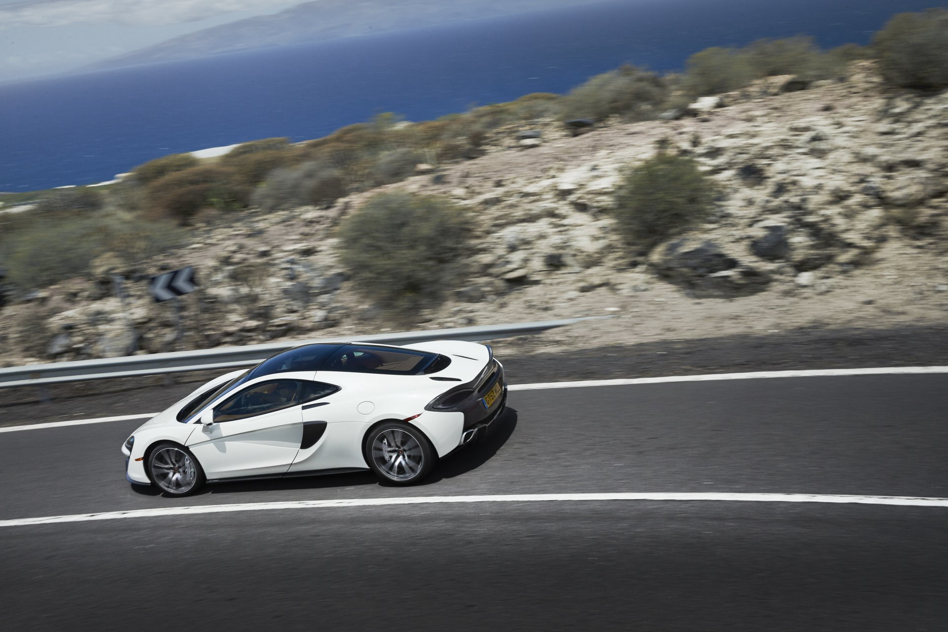 White McLaren 570GT supercar driving on a coastal road, 4K Ultra HD PC desktop wallpaper background.