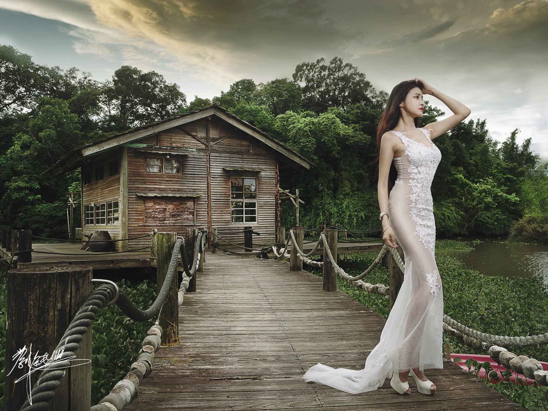 A brunette Asian woman in a white dress poses on a rustic wooden pier next to an old cabin, surrounded by lush greenery. HD desktop wallpaper and background.