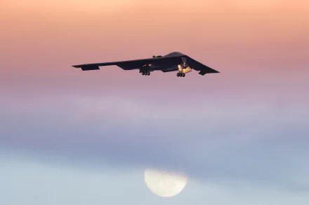 A Northrop B-2 Spirit stealth bomber aircraft from the air force flies against a colorful sunset sky with the moon visible below, captured in 4K Ultra HD.