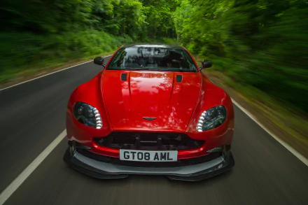Front view of a red Aston Martin Vantage car speeding down a forested road, captured in stunning 4K Ultra HD for a PC desktop wallpaper.
