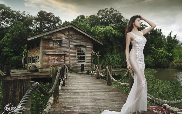 A brunette Asian woman in a white dress poses on a rustic wooden pier next to an old cabin, surrounded by lush greenery. HD desktop wallpaper and background.