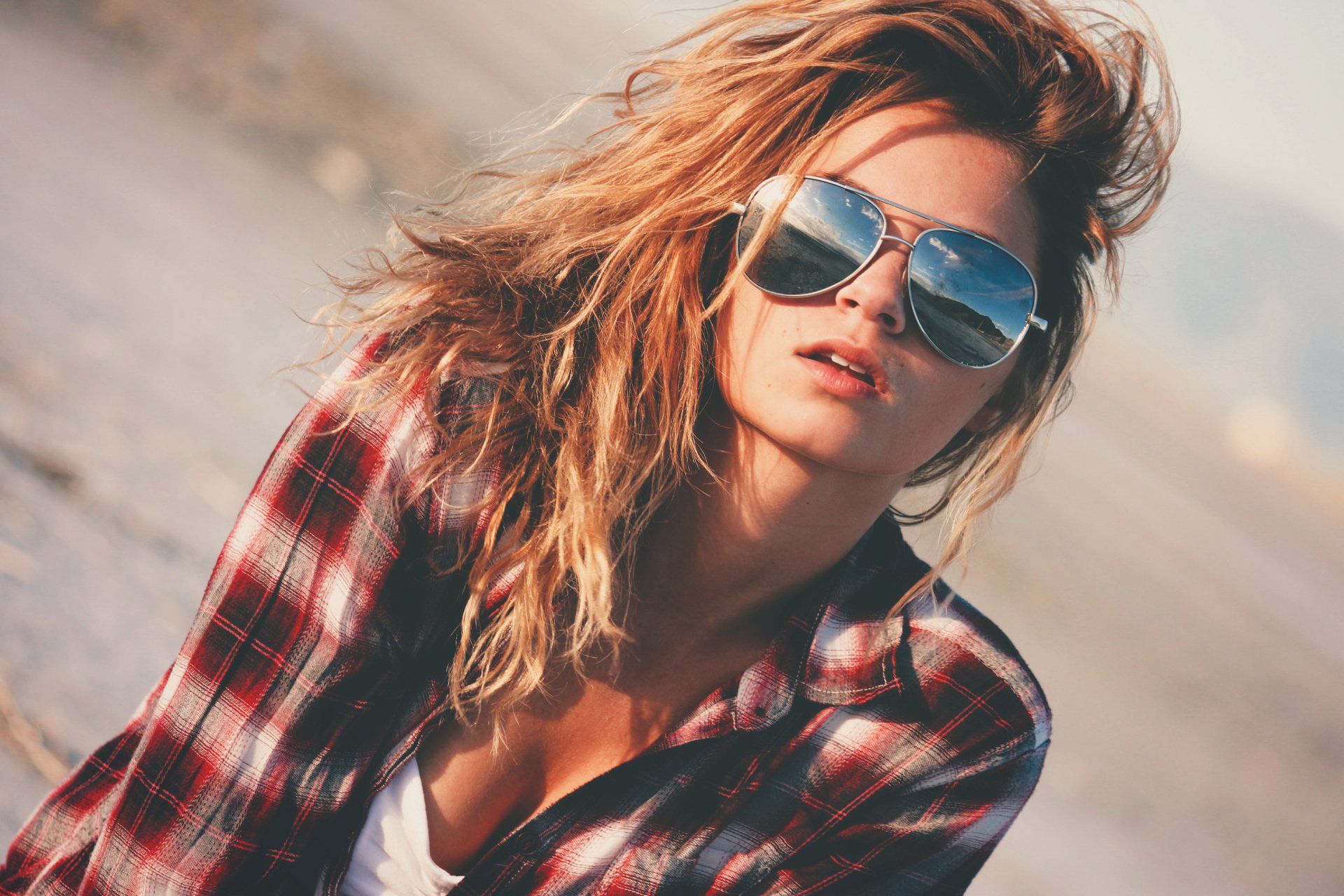 Sunlit brunette woman wearing sunglasses and a plaid shirt, captured in a relaxed, confident mood. HD PC desktop wallpaper and background.
