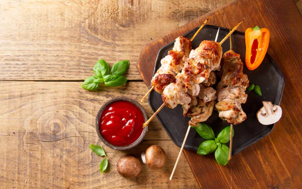 Grilled meat skewers with mushrooms and a bowl of ketchup on a wooden table, styled as a 4K Ultra HD PC desktop wallpaper with barbecue and fresh herbs.