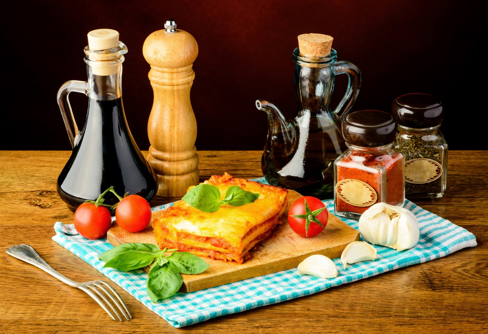 5K Ultra HD PC desktop wallpaper still life of lasagna on a wooden board with oil bottles, pepper mill, tomatoes, garlic and basil — meal food background.