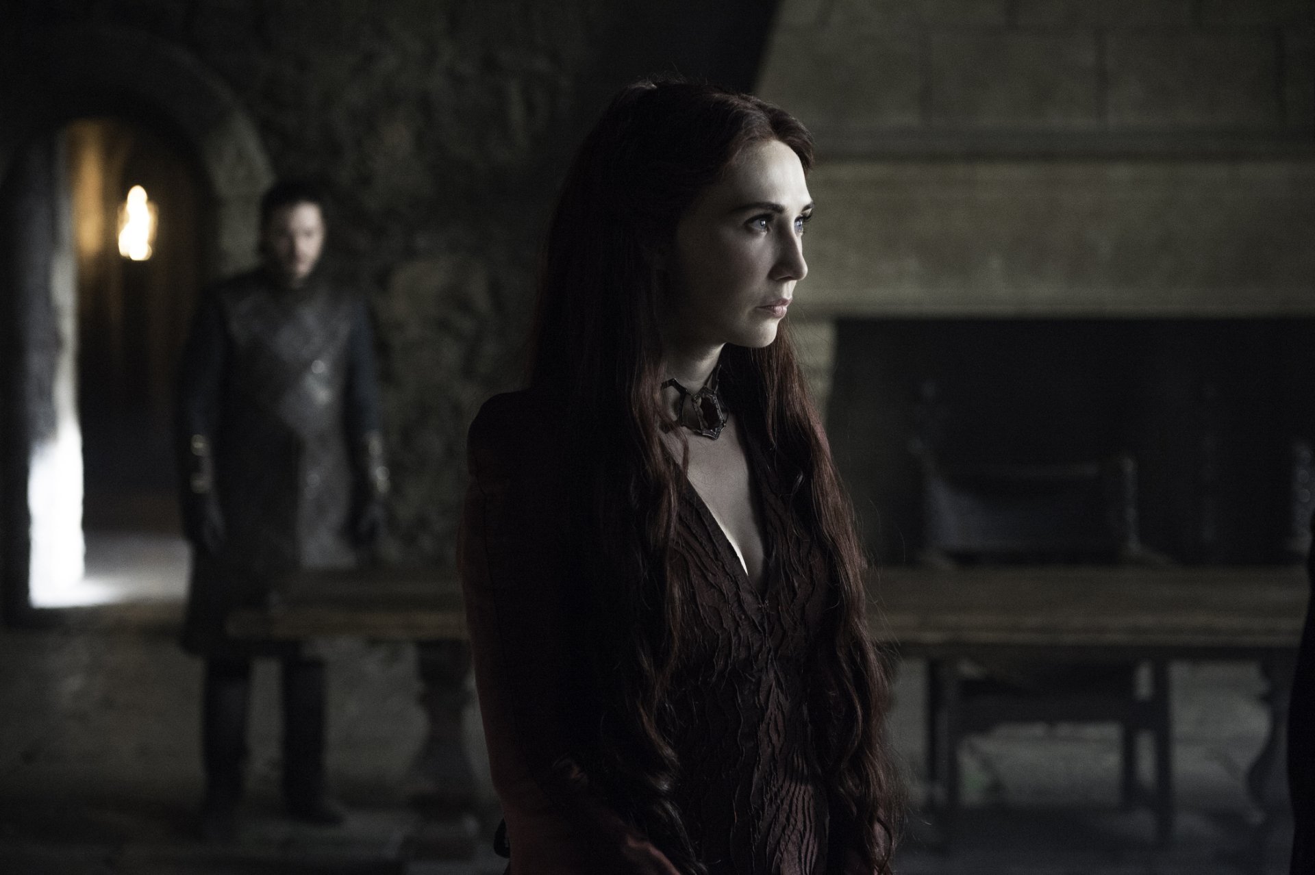 HD desktop wallpaper featuring Carice van Houten as Melisandre from the TV show Game of Thrones in a dimly lit medieval interior.