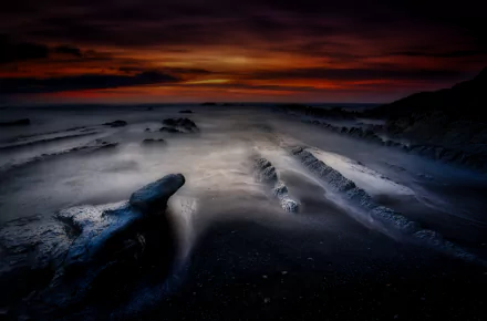 HDR sunset landscape over a dramatic ocean beach; dark rocks and silky tide under a glowing sky — HD PC desktop wallpaper/background.