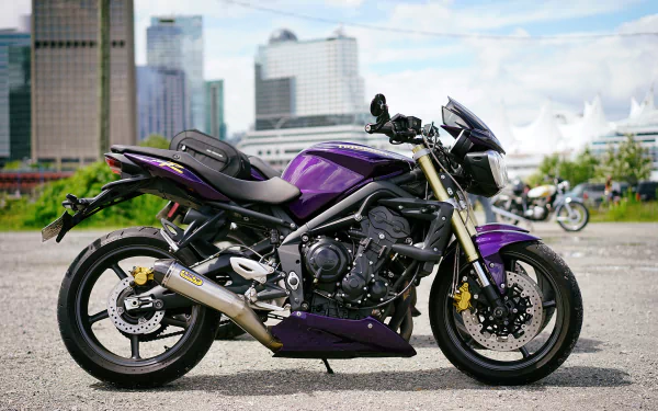 HD desktop wallpaper featuring a sleek purple Triumph motorcycle parked on an urban street with city buildings in the background.