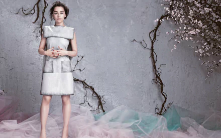 HD PC desktop wallpaper of a brunette English actress and celebrity in a structured silver dress, posed against a textured gray wall with cherry blossoms and pastel tulle.