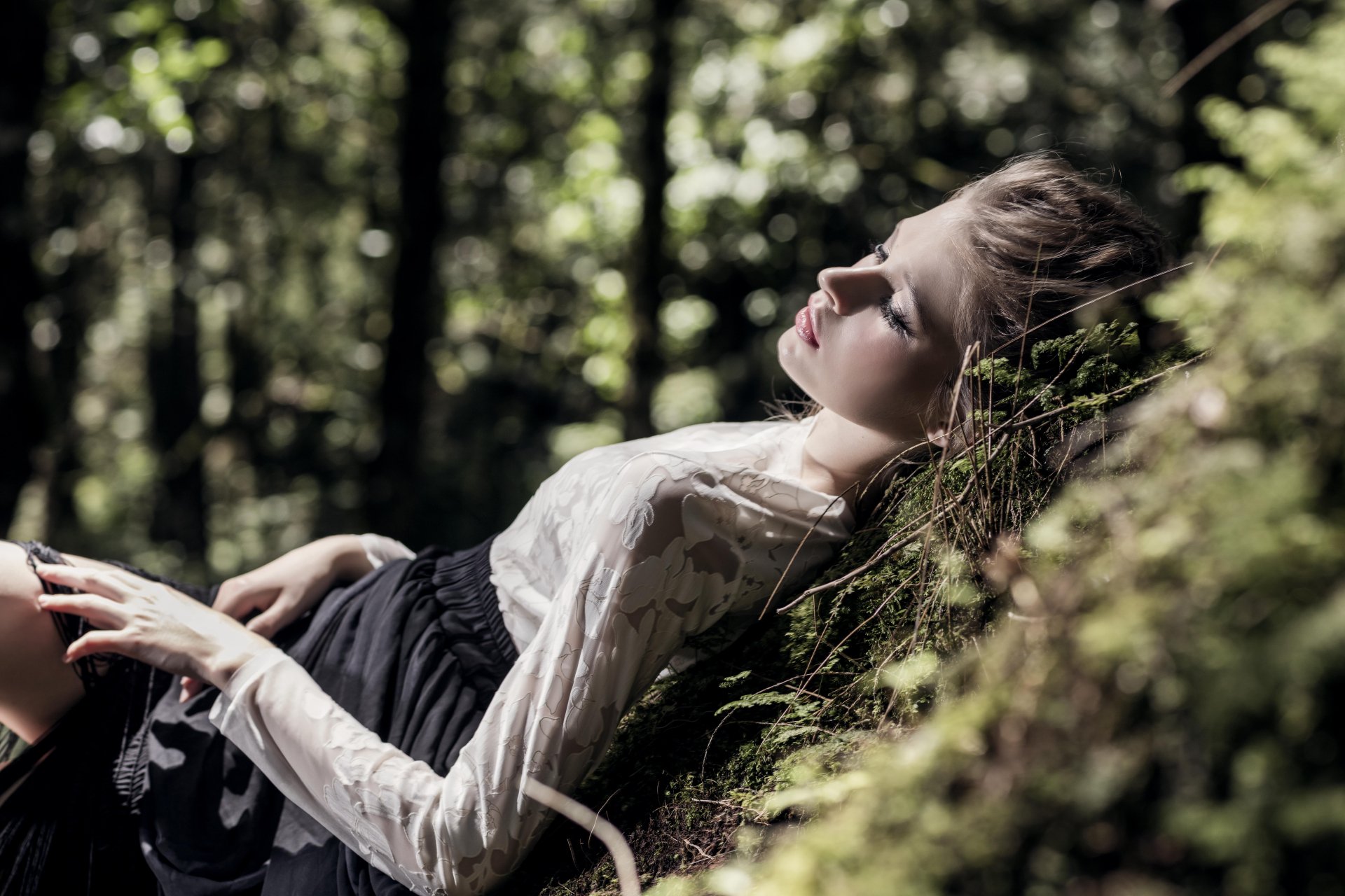 A serene woman model lies down against a mossy surface in a softly lit forest with bokeh, captured in stunning 8K Ultra HD detail for a PC desktop wallpaper.