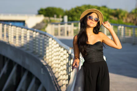 A brunette woman model in a black dress, sunglasses, and hat poses confidently on a sunny day, featured in a high-definition PC desktop wallpaper background.