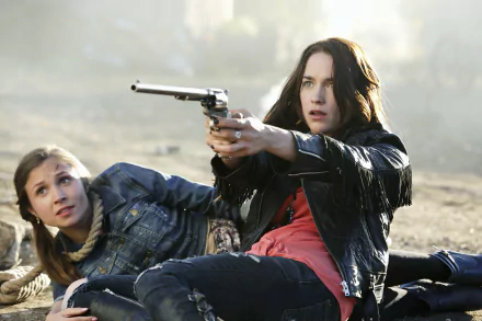 Waverly Earp (Dominique Provost-Chalkley) and Wynonna Earp (Melanie Scrofano) from the TV show Wynonna Earp in an intense outdoor scene aiming a revolver.