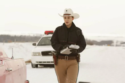Officer Nicole Haught, played by Katherine Barrell in the TV show Wynonna Earp, stands in uniform in front of police cars on a snowy road.