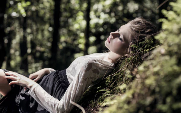 A serene woman model lies down against a mossy surface in a softly lit forest with bokeh, captured in stunning 8K Ultra HD detail for a PC desktop wallpaper.