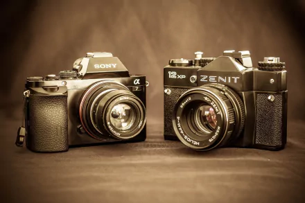 HD desktop wallpaper showing two man-made cameras — a Sony mirrorless with lens beside a vintage Zenit SLR on a warm sepia background.
