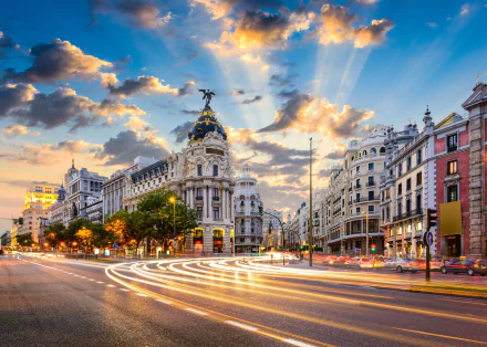 A stunning sunset over Madrid showcases elegant architecture and bustling city life, with vibrant skies and light trails highlighting the square's charm.