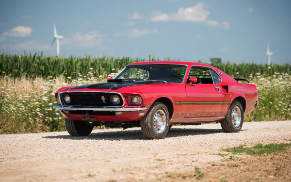 Red Ford Mustang Mach 1 muscle car parked on a dirt road with green fields and wind turbines in the background, captured in 4K Ultra HD.