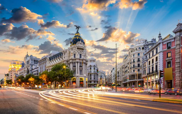 A stunning sunset over Madrid showcases elegant architecture and bustling city life, with vibrant skies and light trails highlighting the square's charm.