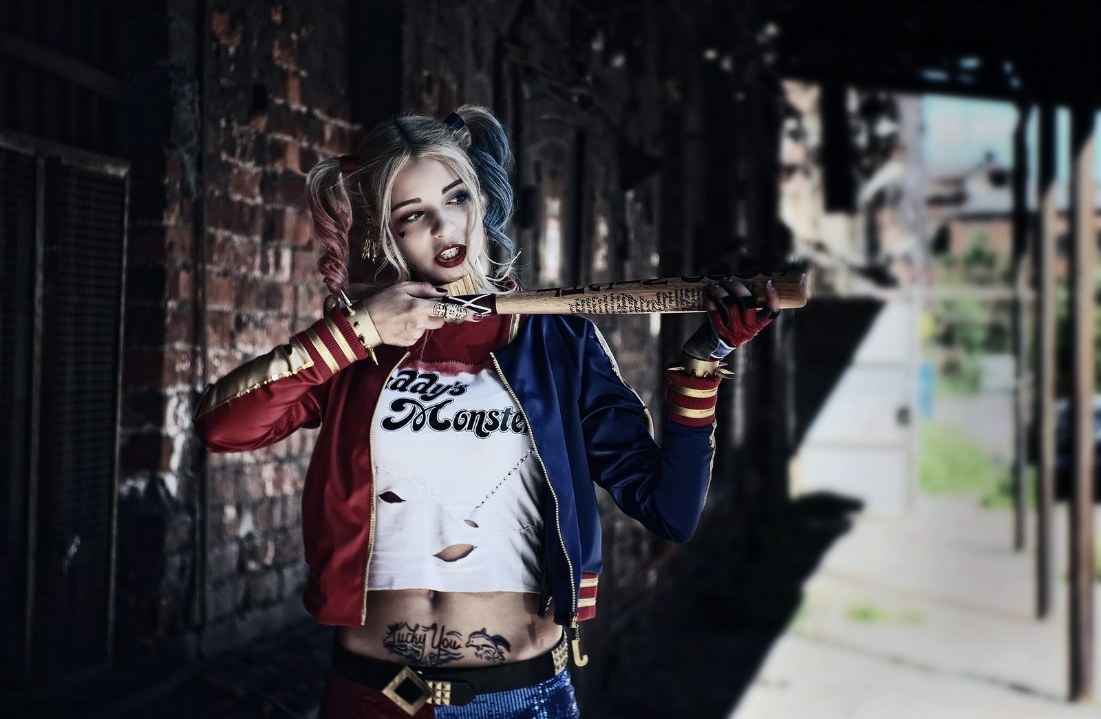 A detailed HD desktop wallpaper featuring a woman in vibrant Harley Quinn cosplay from DC Comics' Suicide Squad, showcasing her playful yet fierce demeanor with a bat.