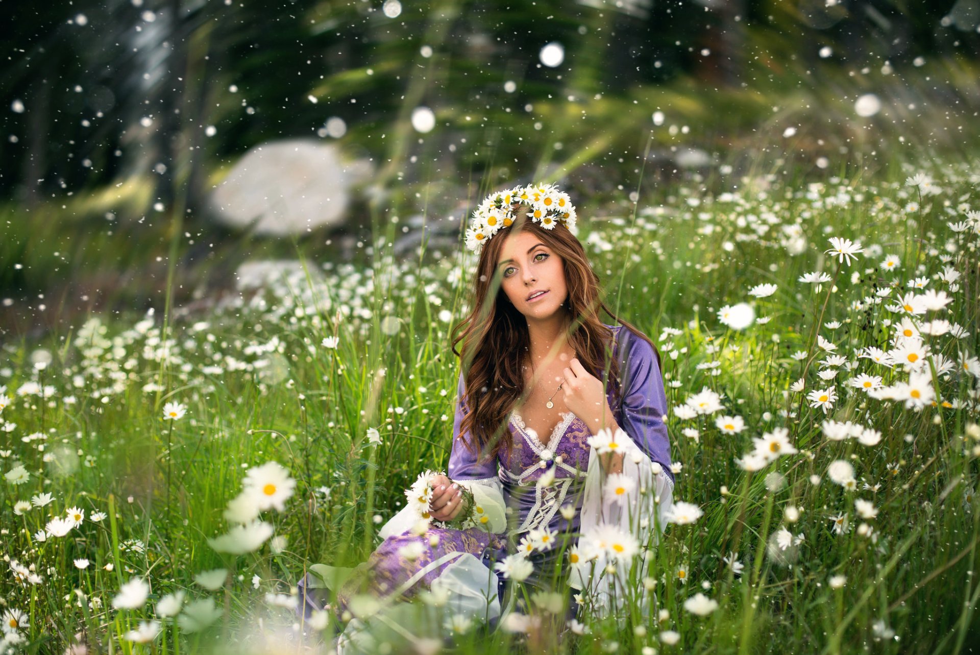 A brunette woman with green eyes and a white flower wreath sits in a blurred outdoor meadow full of white flowers, captured in an HD PC desktop wallpaper style.