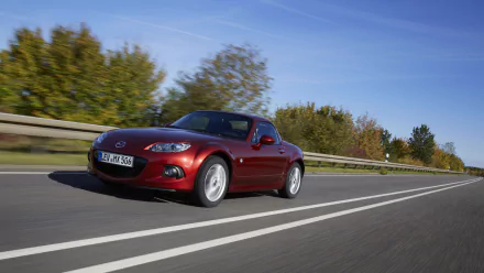 HD desktop wallpaper featuring a red Mazda MX-5 driving on a highway with trees and a clear blue sky in the background.