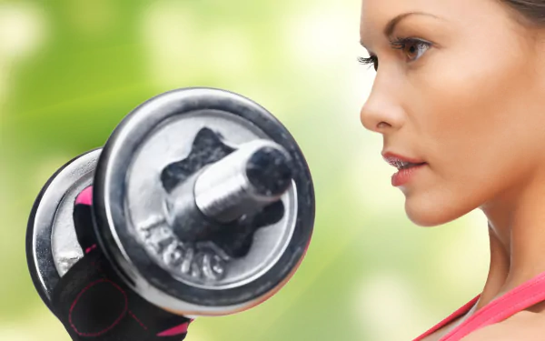 Close-up face of a woman with brown eyes lifting a dumbbell during a sports weightlifting workout — 4K Ultra HD PC desktop wallpaper background.