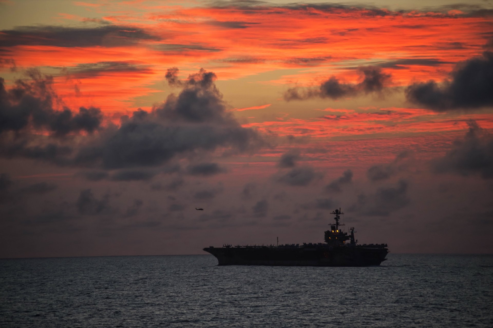 USS John C. Stennis (CVN-74) aircraft carrier silhouette at sea during a vivid orange and red sunset, showcasing the military warship in HD desktop wallpaper quality.
