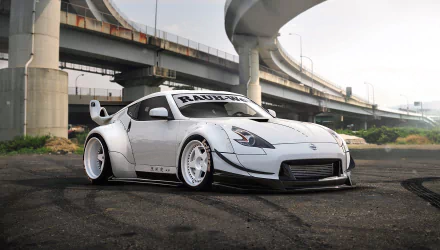 White Nissan 370Z with wide body kit and custom rims parked under an urban overpass, showcased as a high-definition PC desktop wallpaper background.