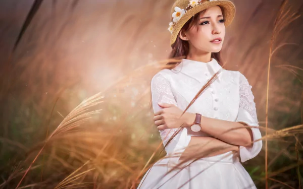 Asian woman with brown eyes and brunette hair wears a white dress and floral hat, posing outdoors in tall grass, captured in sharp 8K Ultra HD quality.