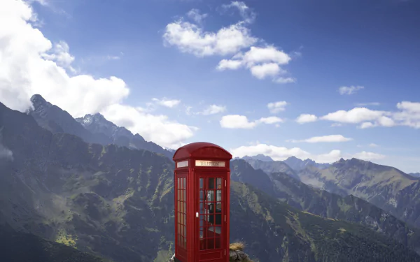 A red phone box stands on a mountain peak under a blue sky with clouds, captured in a 4K Ultra HD manipulated scenic desktop wallpaper.