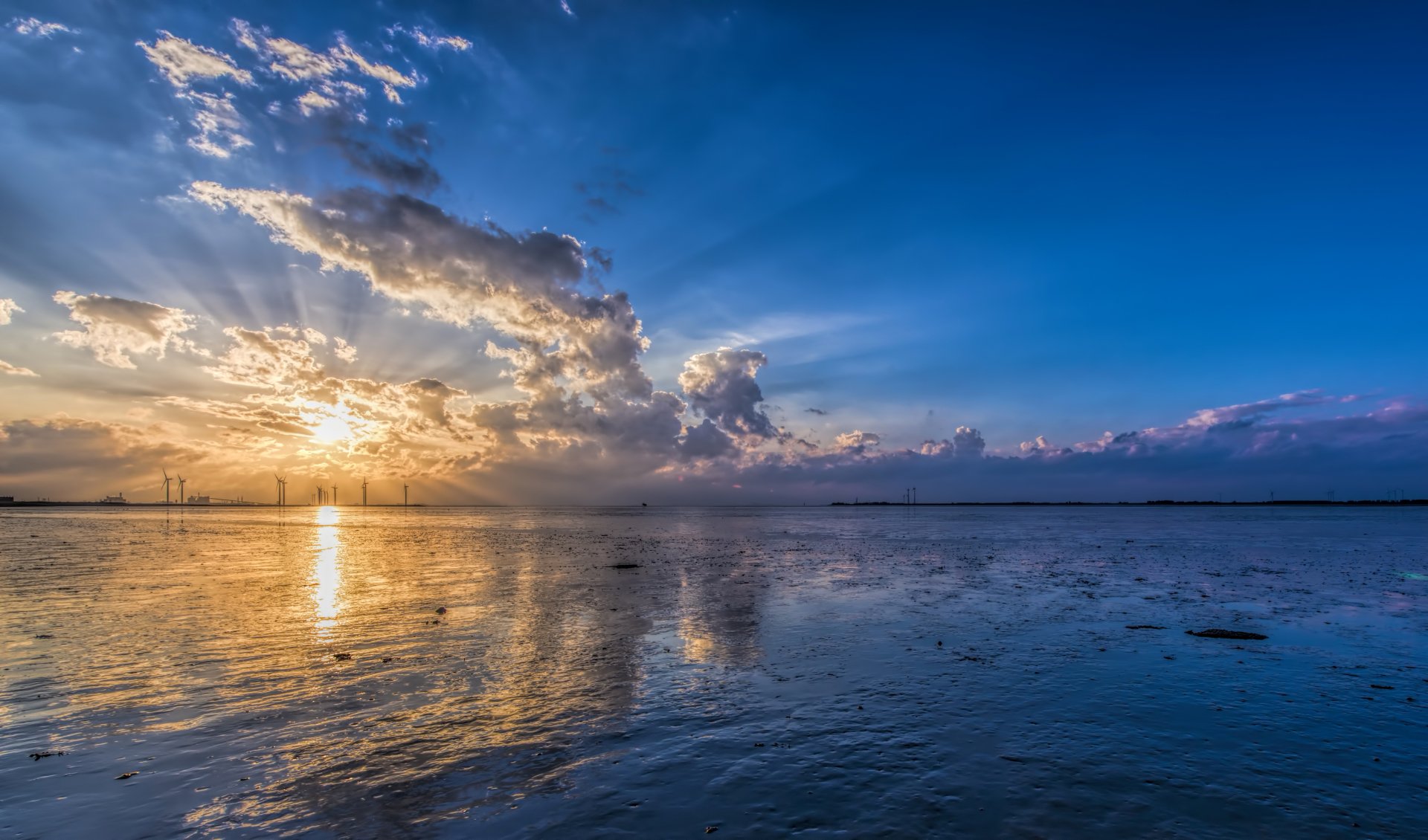 4K Ultra HD desktop wallpaper of sunbeams breaking through clouds over an ocean horizon, with wind turbines reflected on the water under a vibrant sky.