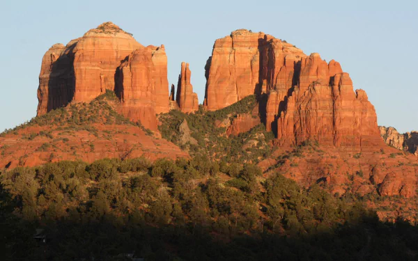 Sunlit red sandstone formations rise above desert vegetation in Sedona, Arizona, showcasing a striking natural landscape in the USA.