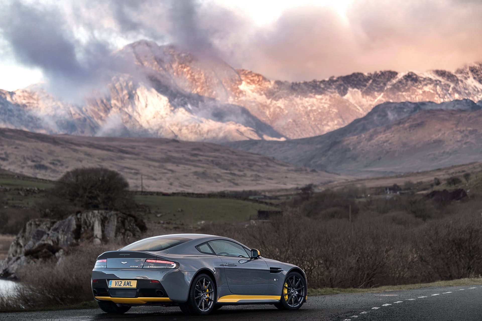 A sleek Aston Martin vehicle parked on a road with dramatic mountain peaks in the background, captured in stunning 4K Ultra HD for a PC desktop wallpaper.