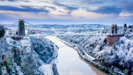 HD desktop wallpaper of the Clifton Suspension Bridge spanning snow-covered cliffs and the River Avon in winter — a man-made landmark in England's landscape.