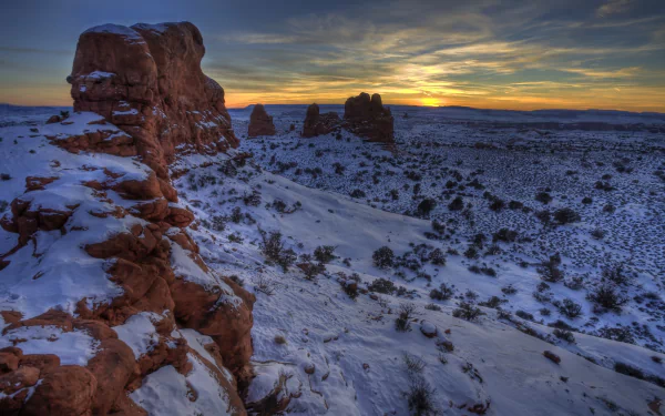 Snow-covered desert landscape at sunset in Arches National Park, Utah, showcasing winter wilderness and vibrant sky colors in an HD nature wallpaper.