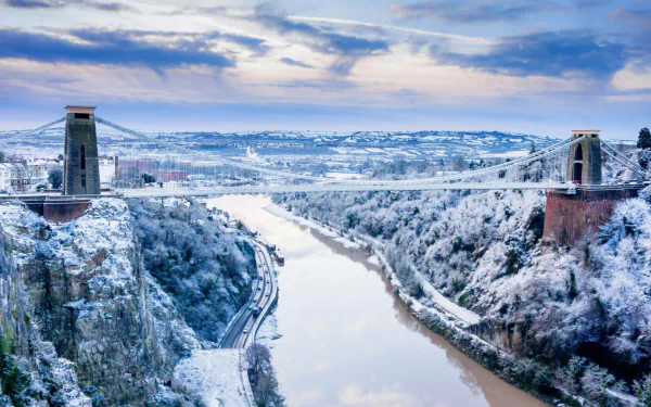 HD desktop wallpaper of the Clifton Suspension Bridge spanning snow-covered cliffs and the River Avon in winter — a man-made landmark in England's landscape.