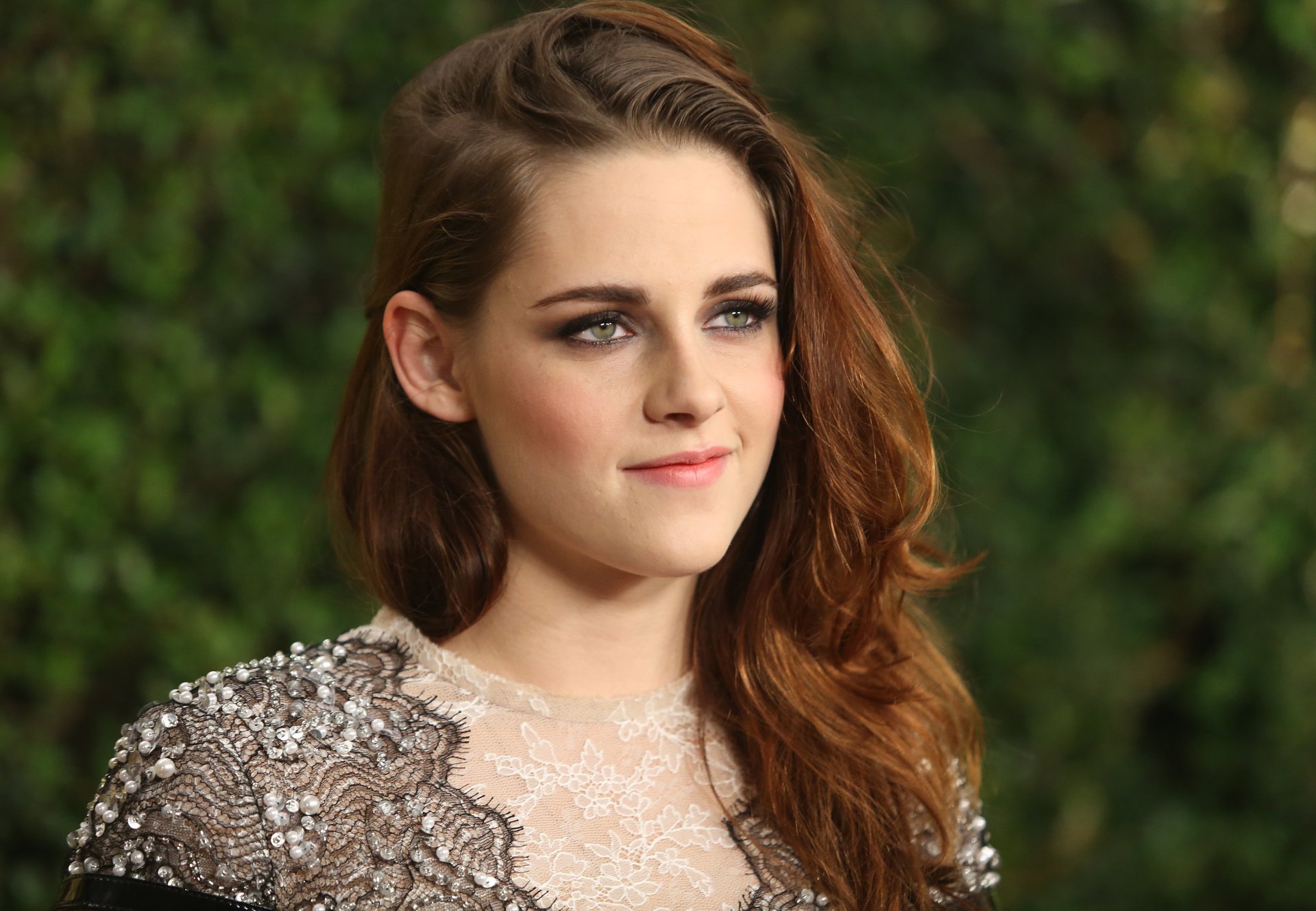 HD wallpaper featuring Kristen Stewart, a talented American actress with brunette hair, captured in a poised moment against a lush green backdrop.