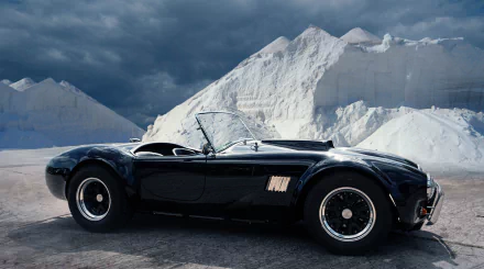 A sleek black AC Cobra sports car parked against dramatic snowy mountain peaks, captured in high-definition for a striking PC desktop wallpaper background.