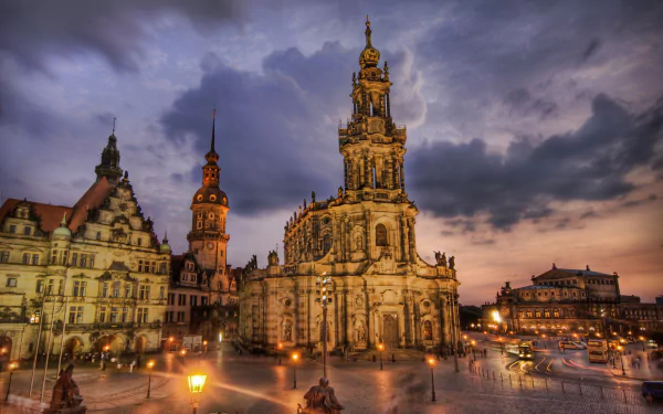 Dusk view of Dresden’s illuminated religious cathedral and surrounding historic architecture in a German square under a dramatic cloudy sky.