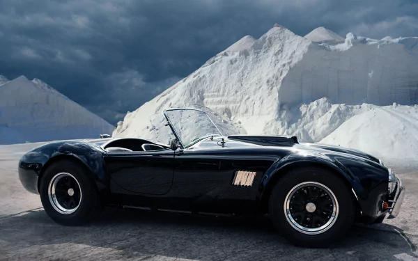 A sleek black AC Cobra sports car parked against dramatic snowy mountain peaks, captured in high-definition for a striking PC desktop wallpaper background.