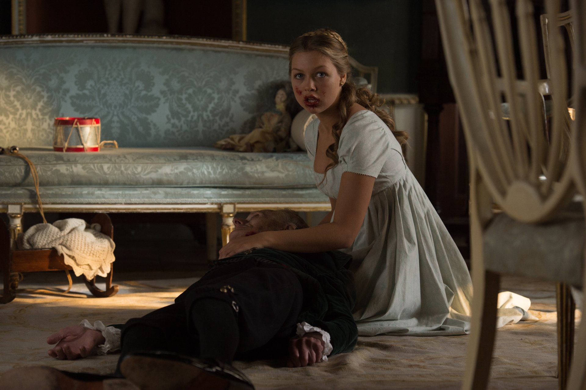 Movie still — Pride and Prejudice and Zombies: a woman in Regency dress kneels beside a fallen man in a dim parlor scene. 4K Ultra HD PC desktop wallpaper/background.