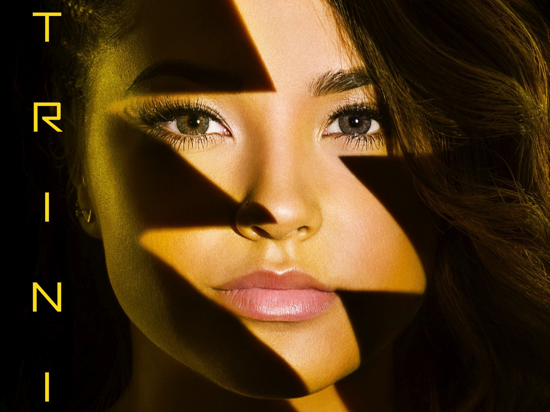 Close-up of Trini Kwan, the Yellow Ranger from the Power Rangers movie (2017), with dramatic lighting highlighting her features, set against a vibrant background.