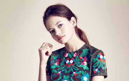 HD desktop wallpaper of a brunette American actress and model Mackenzie Foy with red lipstick, wearing a floral patterned top, posing against a plain background.