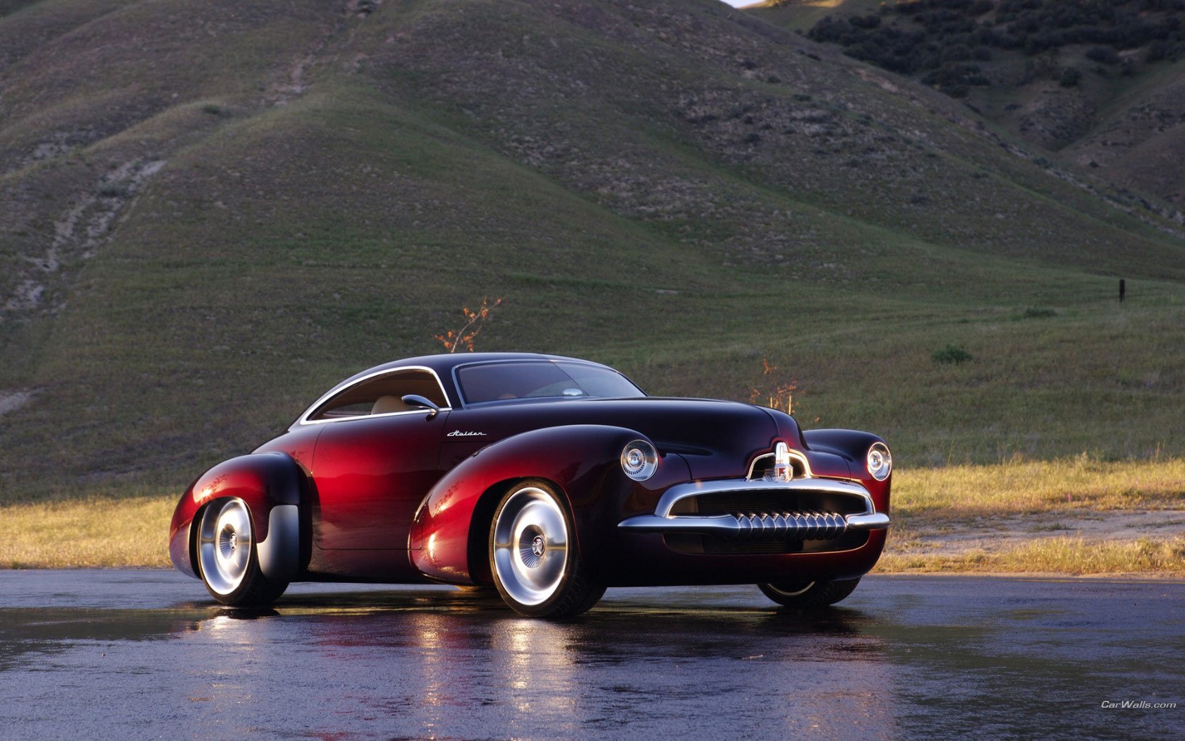 HD PC desktop wallpaper showcasing a classic vehicle, a glossy dark red vintage car parked on a wet surface with rolling hills in the background.