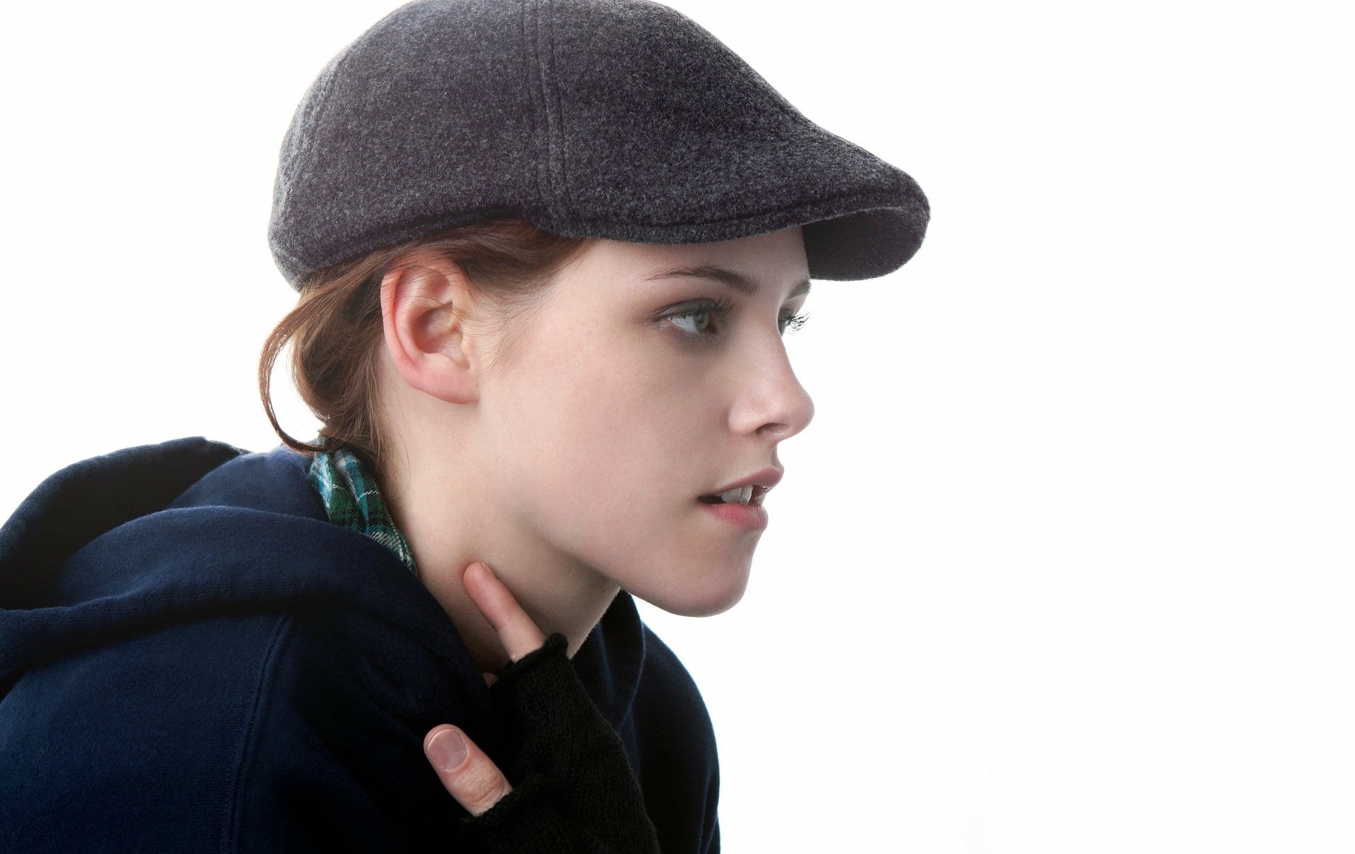 HD PC desktop wallpaper featuring a close-up side profile of celebrity Kristen Stewart wearing a cap and dark clothing against a white background.