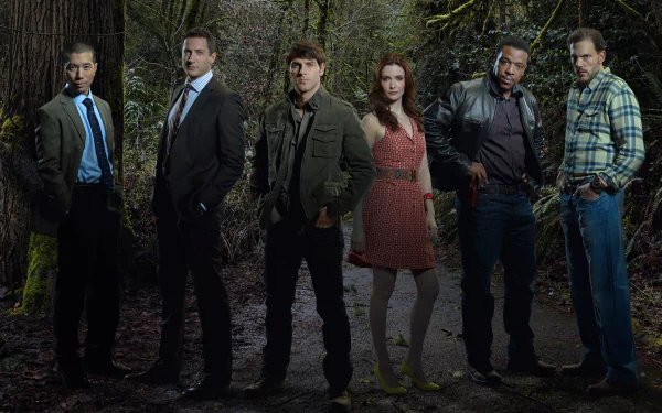 A group of characters from the TV show Grimm, set against a dark, forested background, standing in a line with varied attire, showcasing the show's mysterious atmosphere.