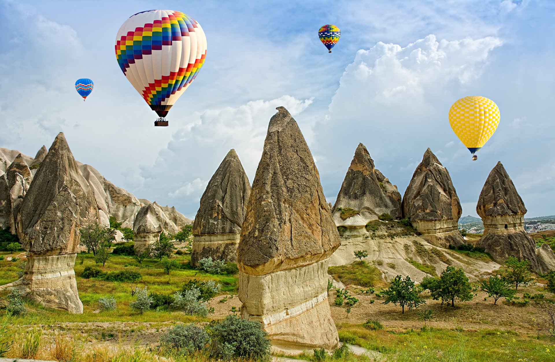 Colorful hot air balloons float over unique rock formations under a blue sky with clouds in Turkey, captured in stunning 4K Ultra HD.